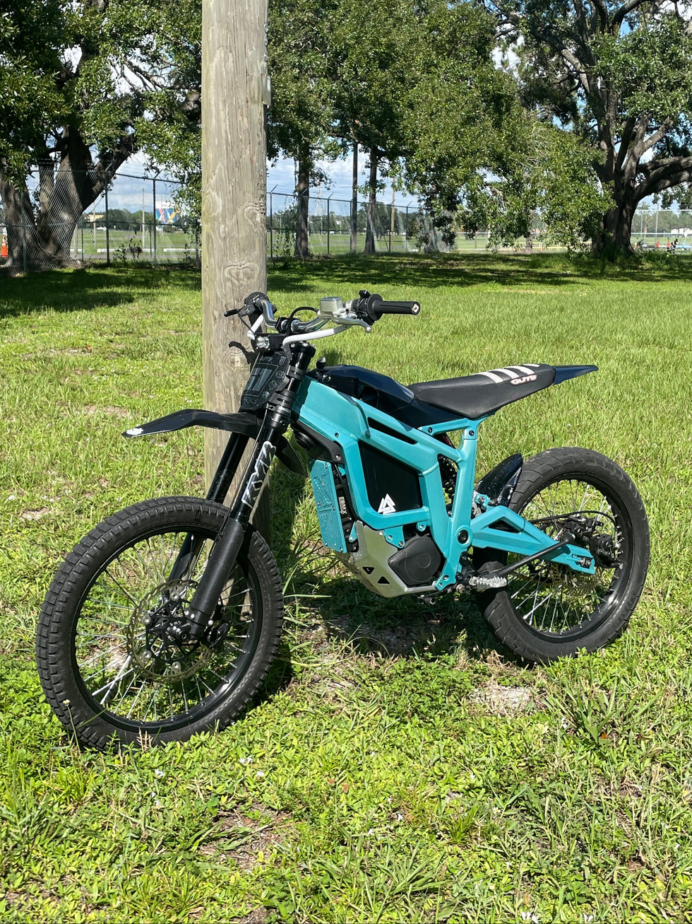 Blue dirt bike parked on grass with trees in the background